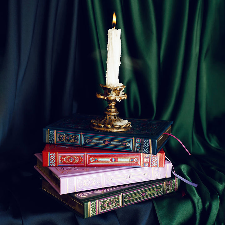 Literati Journals - Set of 4 - The Quirky Cup Collective - Four decorative and gilded classically designed journals in green, purple, blue and red. Stacked with their covers and spines against a silk background with a brass gold candelabra