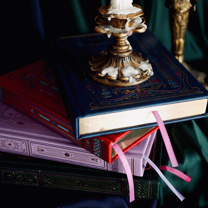 Literati Journals - Set of 4 - The Quirky Cup Collective - Four decorative and gilded classically designed journals in green, purple, blue and red. Stacked with their covers and spines against a silk background with a brass gold candelabra