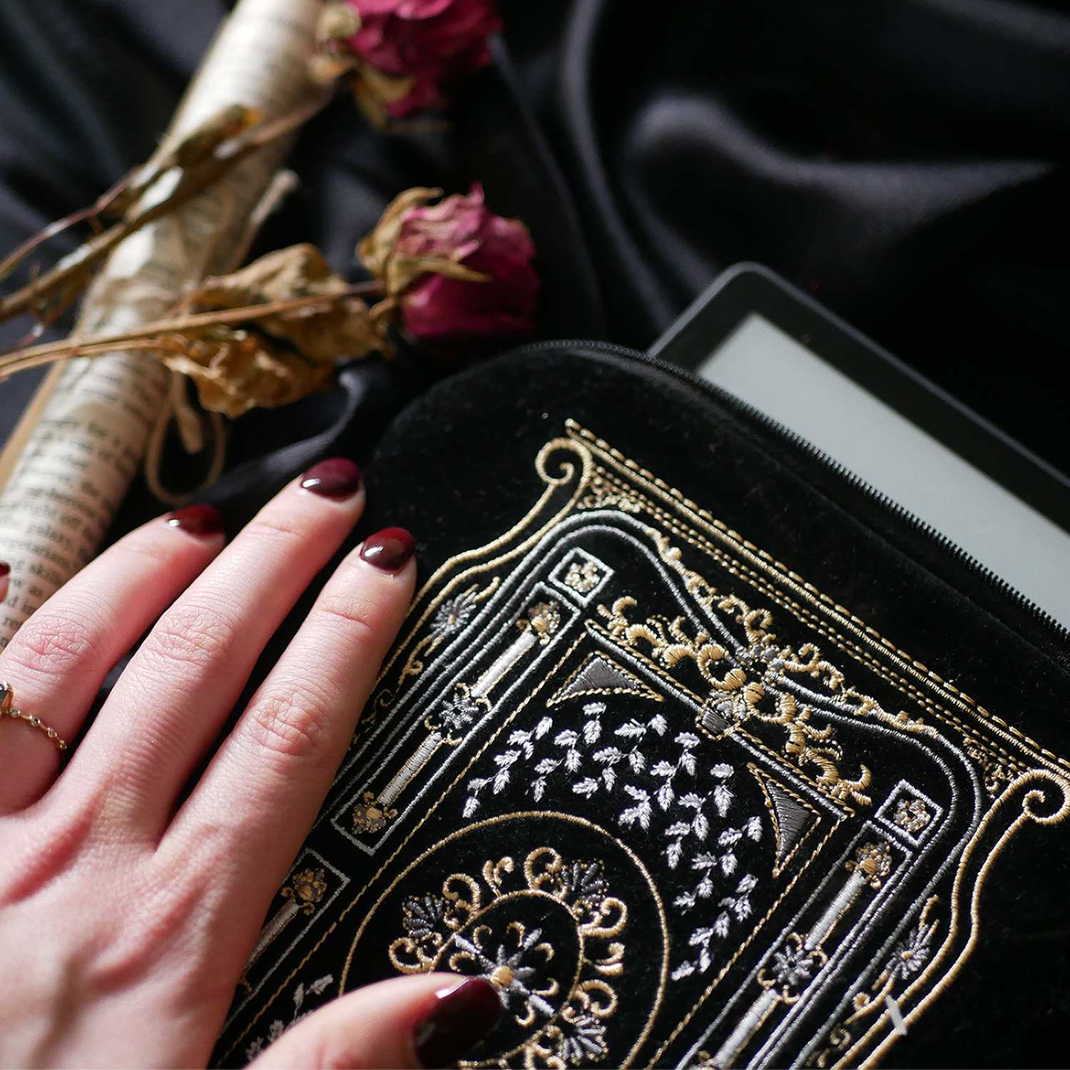 Black literati eReader sleeve features white and gold embroidered detail in an intricate classical book style. The black velvet kindle case sits on a black fabric background.