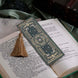 The sage green literati bookmark features a classical book inspired design with intricate gold foiling and a soft gold tassel. The bookmark sits on a classical book on a soft green fabric background.