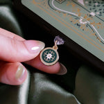 On a sage green background a hand holds an eReader with the Sage green Literati dust plug inserted into it. The gold and green enamel circular design is plugged into the device that has a matching sage green eReader sticker insert.