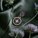 On a sage green background surrounded by flowers sits the Sage green Literati dust plug. The gold and green enamel circular design features a floral motif inspired by classical Victorian books.