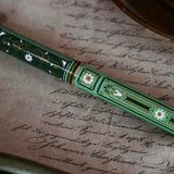 Detail image of the sage green Bibliophile pen by The Quirky Cup Collective. The light green pen features a classic book inspired design in shades of green, white and cream with gold detailing. The pen sits on a letter with intricate cursive handwriting.