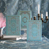 The 3 aqua Antionette journals and reading journals sit together on a light blue tablecloth surrounded by candles, pearls and pink features. The intricate foil covers in shades of pink, gold and blue reference the designs of Victorian book aesthetic for the perfect elevated journaling experience.