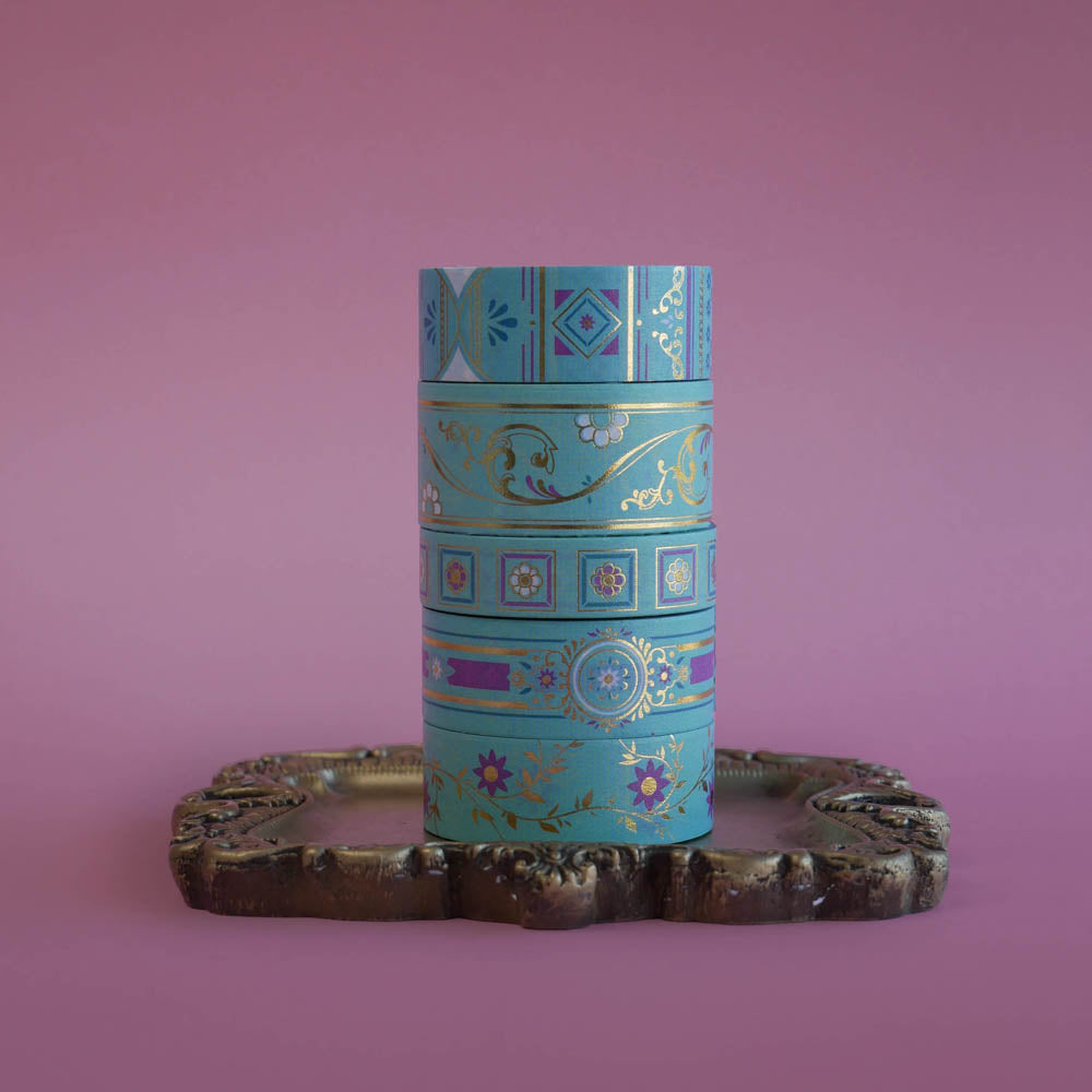 A detail of a stack of the french inspired washi tape included in the Antoinette set. The romantasy aesthetic light blue washi tape designs are inspired by classical books and feature floral motifs in shades of pink, blue and gold foil.