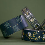 A close up of full set of the Sage green variations of the Literati washi tape by The Quirky Cup Collective sit as rolls in piled stack in a green background. The classic book inspired washi tape designs feature classical book inspired designs and ornamentation in shades of dark green, sage green, white and foiled gold.
