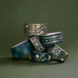 The full set of the Sage green variations of the Literati washi tape by The Quirky Cup Collective sit as rolls in piled stack in a green background. The classic book inspired washi tape designs feature classical book inspired designs and ornamentation in shades of dark green, sage green, white and foiled gold.