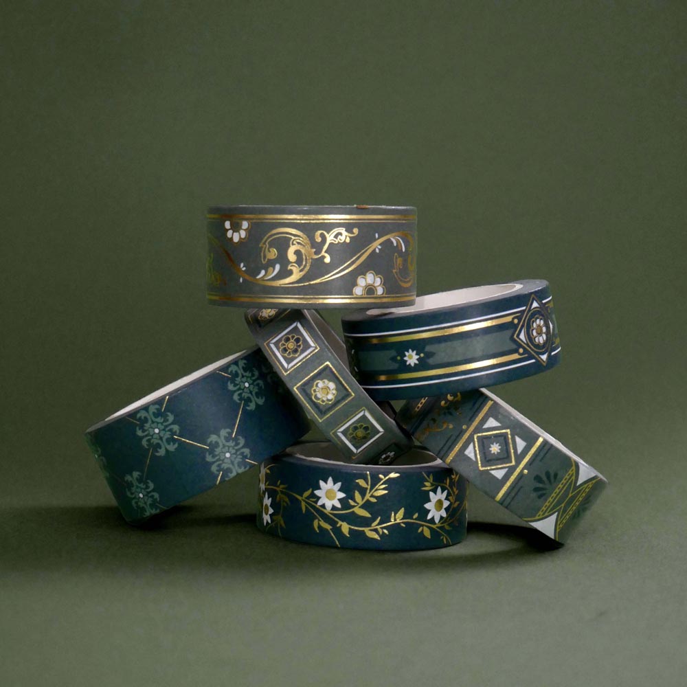 The full set of the Sage green variations of the Literati washi tape by The Quirky Cup Collective sit as rolls in piled stack in a green background. The classic book inspired washi tape designs feature classical book inspired designs and ornamentation in shades of dark green, sage green, white and foiled gold.