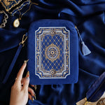 The Moncherie eReader and kindle case by The Quirky Cup Collective is the perfect feminine kindle aesthetic addition for book lovers. The blue velvet case features an intricate French inspired design in shades of gold, cream and light blue. The case also features a wrist strap with gold hardware. The case is styled on a royal blue fabric background and is surrounded by blue bookish props.