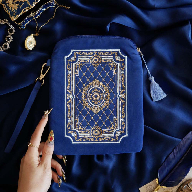 The Moncherie eReader and kindle case by The Quirky Cup Collective is the perfect feminine kindle aesthetic addition for book lovers. The blue velvet case features an intricate French inspired design in shades of gold, cream and light blue. The case also features a wrist strap with gold hardware. The case is styled on a royal blue fabric background and is surrounded by blue bookish props.