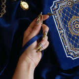 The Moncherie eReader and kindle case by The Quirky Cup Collective is the perfect feminine kindle aesthetic addition for book lovers. The blue velvet case features an intricate French inspired design in shades of gold, cream and light blue. The case also features a wrist strap with gold hardware, here being held by a hand with intricate gold nails. The case is styled on a royal blue fabric background and is surrounded by blue bookish props.