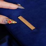 The Moncherie eReader and kindle case by The Quirky Cup Collective is the perfect feminine kindle aesthetic addition for book lovers. The blue velvet case features an intricate French inspired design in shades of gold, cream and light blue. The case also features a wrist strap with gold hardware and gold logo back plate, here being held by a hand with intricate gold nails. The case is styled on a royal blue fabric background and is surrounded by blue bookish props.