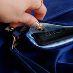 The Moncherie eReader and kindle case by The Quirky Cup Collective is the perfect feminine kindle aesthetic addition for book lovers. The blue velvet case features an intricate French inspired design in shades of gold, cream and light blue. The case also features a wrist strap with gold hardware and a light blue satin interior, here being shown held open by hands with intricate gold nails. The case is styled on a royal blue fabric background and is surrounded by blue bookish props.