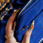 The Moncherie eReader and kindle case by The Quirky Cup Collective is the perfect feminine kindle aesthetic addition for book lovers. The blue velvet case features an intricate French inspired design in shades of gold, cream and light blue. The case also features a wrist strap with gold hardware, here being held by a hand with intricate gold nails. The case is styled on a royal blue fabric background and is surrounded by blue bookish props.