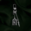 The silver Night Realm Charmlet (A mix and match accessory for decorating your romantasy kindle aesthetic) by The Quirky Cup Collective sits on a green fabric background. The design featured a silver clasp and multiple charms hanging from different length detachable chains including an arched stained glass window with moon and star motifs, a sword and a star.