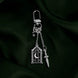 The silver Night Realm Charmlet (A mix and match accessory for decorating your romantasy kindle aesthetic) by The Quirky Cup Collective sits on a green fabric background. The design featured a silver clasp and multiple charms hanging from different length detachable chains including an arched stained glass window with moon and star motifs, a sword and a star.