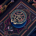 The blue oath Breaker clingie (think a bookish enamel pop socket!) is attached to a kindle with a matching navy eReader insert sticker. The Clingie design centers on a crown, sword and snake motif with two hands at the bottom. The mostly circular (the bottom has a 'notch' Clingie is in shades of navy, teal, white and rich berry pink alongside the gold enamel. The insert sticker features a similar design with more snakes and geometric detailing.
