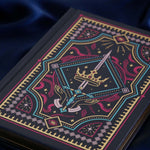 The navy blue Oath Breaker journal features an intricate cover foiled with shades of bright pink,, hold, teal and light pink. Motifs of snakes, crowns, swords, eyes and hands make for the perfect fantasy inspired gift. The journal sits on a royal blue fabric background.