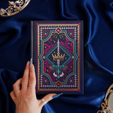 The navy blue Oath Breaker journal features an intricate cover foiled with shades of bright pink,, hold, teal and light pink. Motifs of snakes, crowns, swords, eyes and hands make for the perfect fantasy inspired gift. The journal sits on a royal blue fabric background and is held by a hand.