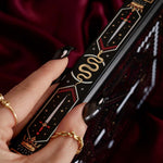 Decorative dark fantasy journal book spine with intricate designs held by a hand wearing gold rings.