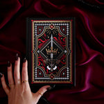 Decorative foiled journal with an intricate dark fantasy design held by a hand on a dark fabric background