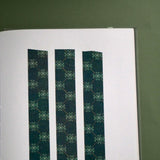 The Sage green variation of the Ornate Literati washi tape sits as three strips stuck to a white journal page on a green background with the ornate wallpaper inspired design in shades of dark green, sage green and gold.