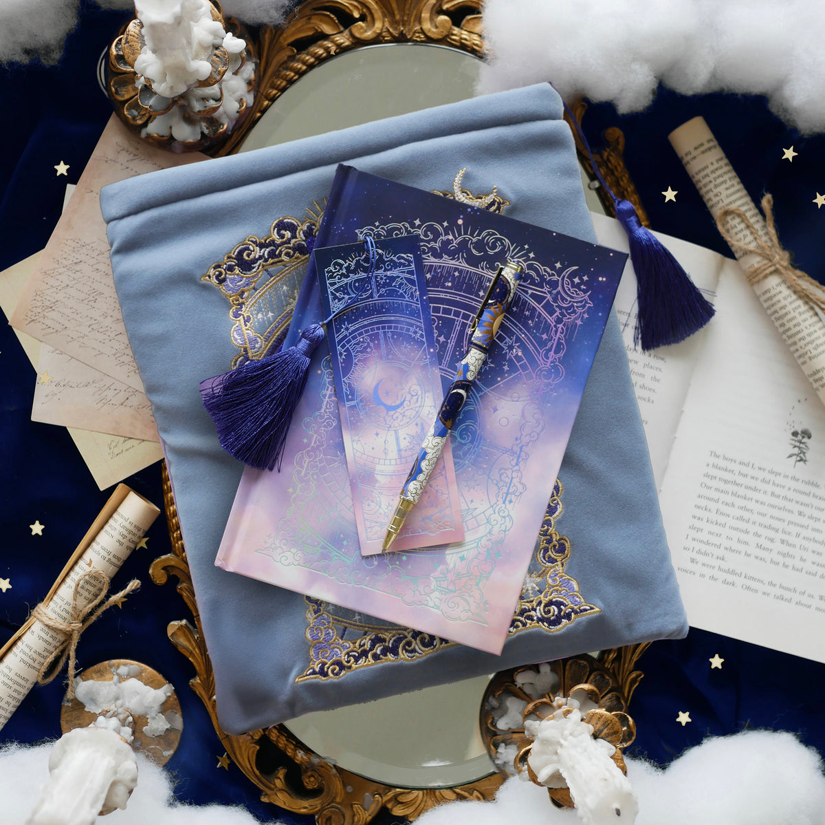 Bundle of stationery products sitting on whimsical celestial inspired background. Items include a blue celestial inspired bookmark, pen, journal and book sleeve. 