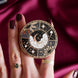 Hand holding a decorative kindle grip with celestial design against a pink fabric background