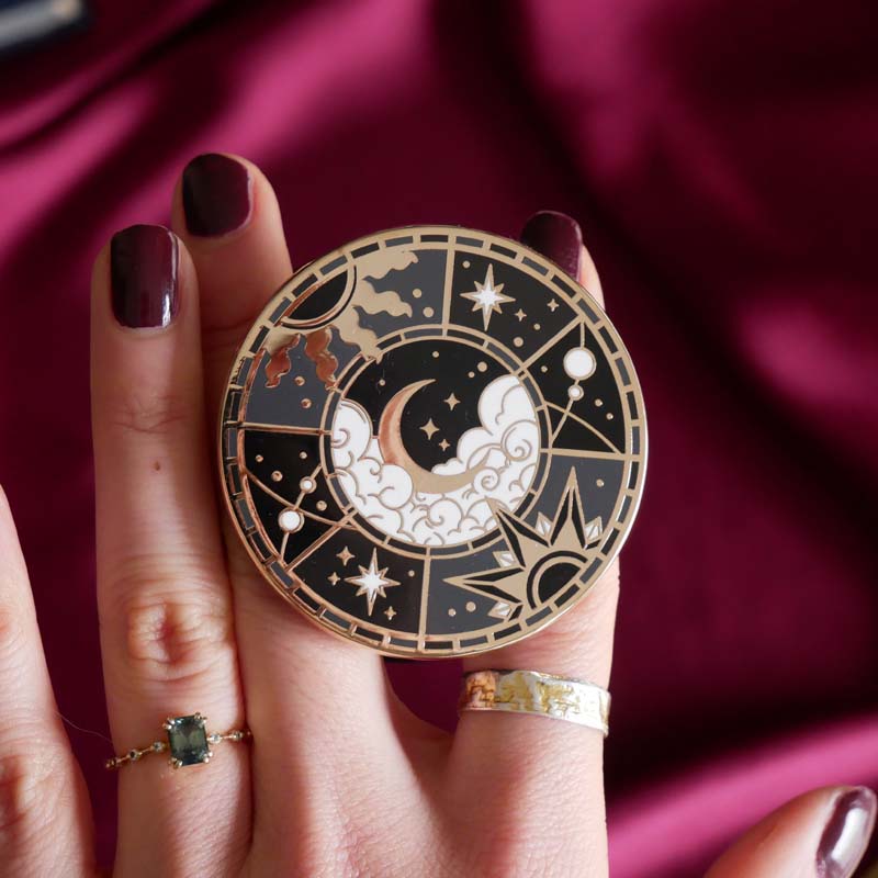 Hand holding a decorative kindle grip with celestial design against a pink fabric background