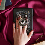 Hand holding a decorative kindle grip with celestial design against a pink fabric background