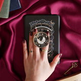 Hand holding a decorative kindle grip with celestial design against a pink fabric background
