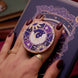 Hand holding a decorative kindle grip with intricate purple and moon designs with gold accents on a dark kindle background