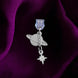 An detail shot of the silver Otherworldly dust plug on a deep purple fabric background. The book inspired dust plug is feature two charms- a planet wth rings around it and a small star attached via a chain.