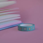 The Poetica design of French inspired washi tape as part of the Antoinette collection sits on a light pink background. The feminine washi tape features geometric flower motifs in shades of blue, pink and foil gold.