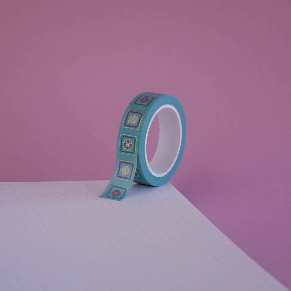 The Poetica design of French inspired washi tape as part of the Antoinette collection sits on a light pink background. The feminine washi tape features geometric flower motifs in shades of blue, pink and foil gold.