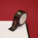 A close up of the Prophecy Foretold washi tape by The Quirky Cup Collective. The roll of fantasy inspired washi tape is on the corner of a white journal on a red background. The bookish washi tape design is black with red and gold detailing- the intricate design showing a crown, red snake, goblet and star icons.