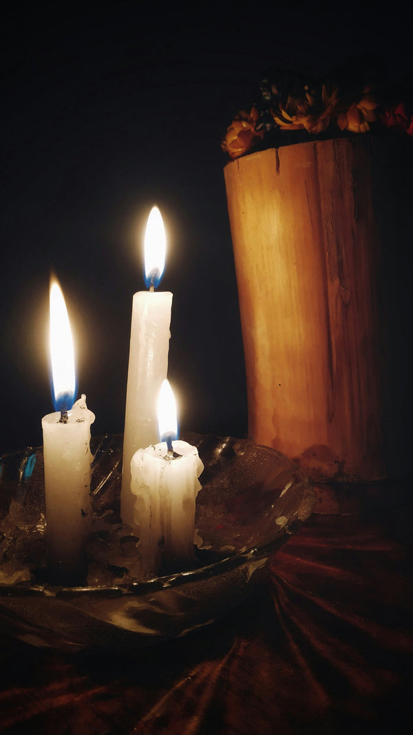 An inspiration image for The Quirky Cup Collective's 'Serpents and Swords'. collection. A set of three candles is alight in front of a wooden pillar in a dark room.