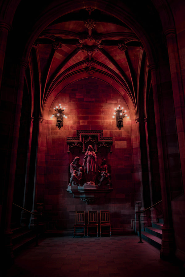 An inspiration image for The Quirky Cup Collective's 'Serpents and Swords'. collection. A dark cathedral interior with religious sculpture on a wall is bathed in red toned lights.
