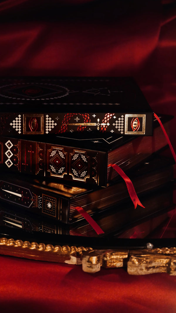 On a red backdrop sits the stack of journals by The Quirky Cup Collective as part of their Serpents & Swords collection. The black journals have red ribbons and intricate foiling in red, gold and white.