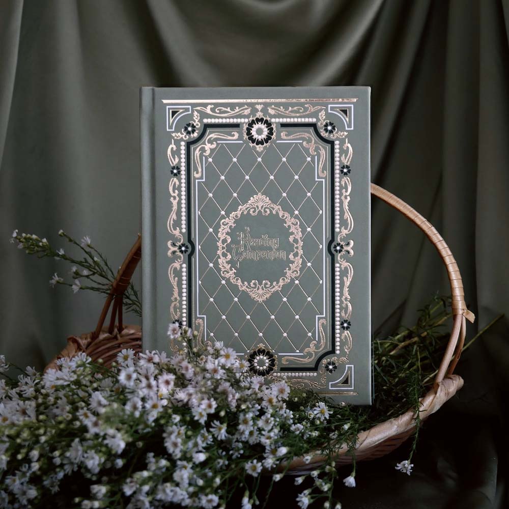 A close up of the sage green Reading Companion Journal. The journal features gold gilded page edges and an  intricate gold, green and white foiling with it's cover design inspired by classical books and a love of reading.