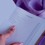 A spread of the Wisteria Lilac Reading journal by The Quirky Cup Collective sits on a soft lilac background with pearls and a dreamy, hazy aesthetic. The page shown is the contents showing the inclusions of the journal such as a welcome, Reading Goals, Reading Tracker, reading Challenges, TBR list, wishlist and quick and full reviews.