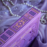 The spine of the highly decorative purple reading Journal by The Quirky Cup Collective sits surrounded by pearls in soft purple fabric. In a soft lilac colour, the spine featured classic-inspired ornamentation with gold foil accents for a romantasy inspired reading journal that feels bold and high end.