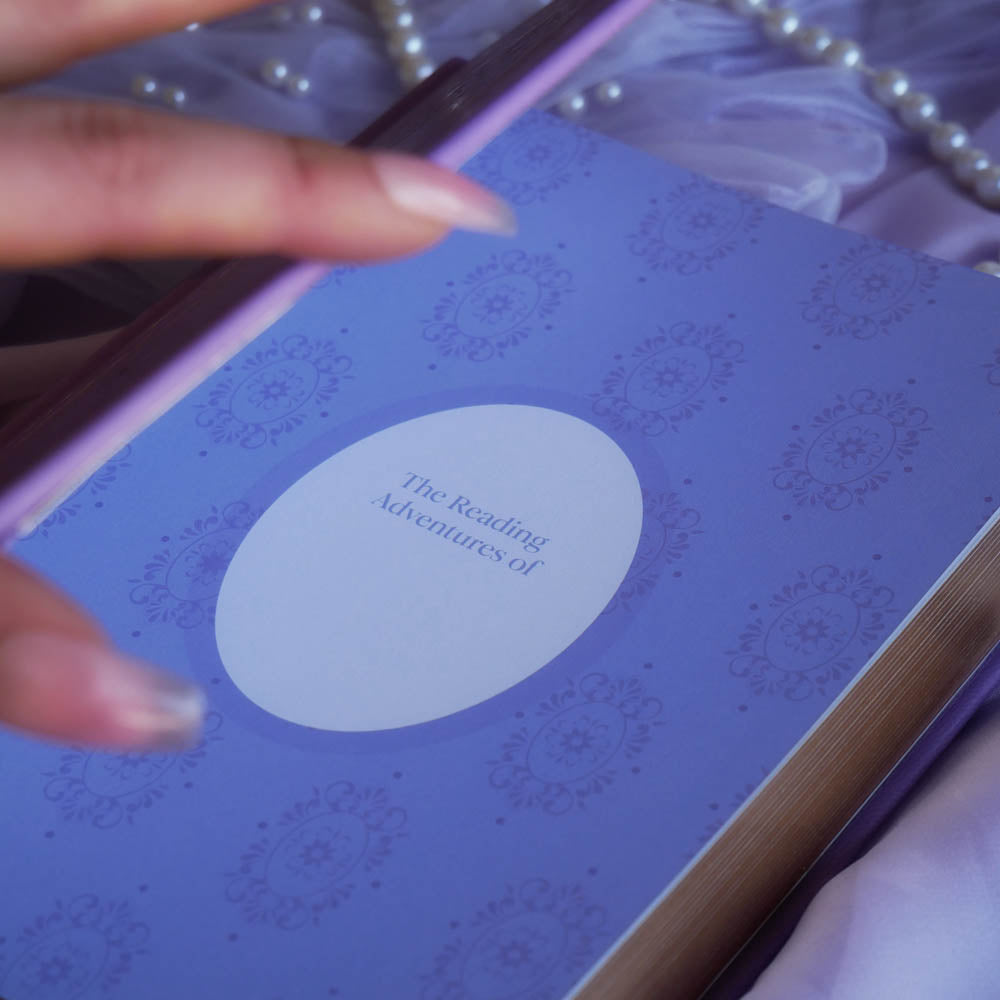 A spread of the Wisteria Lilac Reading journal by The Quirky Cup Collective sits on a soft lilac background with pearls and a dreamy, hazy aesthetic. The page is the opening page of the fantasy inspired reading journal and is mostly lilac with a name plate.