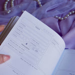 A spread of the Wisteria Lilac Reading journal by The Quirky Cup Collective sits on a soft lilac background with pearls and a dreamy, hazy aesthetic. The page shown  i s the full review page with space for the fantasy reader to note the book details, their rating and their opinion of the book.