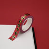 A close up of the Royal Decree washi tape by The Quirky Cup Collective. The roll of fantasy inspired washi tape is on the corner of a white journal on a red background. The bookish washi tape design is primarily red with black and gold detailing- the intricate design showing a gold crown.