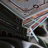 A detail image of the Sage trilogy of journals includes the standard journal, reading journal and reading companion by The Quirky Cup Collective in the sage Literati colour variation. Each journal features intricate gold foil detailing with gilded gold paper edges. The journals sit in front of a sage green fabric background.