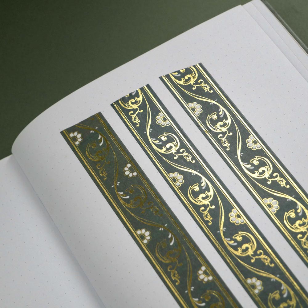 The Sage green variation of the Scriptus Literati washi tape. The classic book inspired washi tape design sits as three strips on a journal page and is shown on a green background and features a classic victorian motif of flowers and curling scrolls in shades of dark green, sage green, white and foiled gold.
