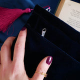 The back of the blue Serpents & Swords book sleeve. The velvet book case is a rich deep blue and features a bright pink tassel, the case held by a hand with purple nails over a blue fabric background.