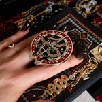 A detail of the Serpents & Swords eReader decor bundle. On a chess board on a black background a hand holds the oath Breaker clingie (think an enamel pop socket!), attached to a kindle with matching eReader sticker insert. It sits on the matching eReader case and has a matching charmlet attached. The range features snake, crown and sword motifs and is black with gold, red and white detailing.