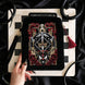 The Serpents & Swords eReader sleeve sits on a chessboard on a black fabric background surrounded by black snakes. The velvet kindle case features snake, crown and sword motifs and is black with gold, red and white detailing. he case also features a wrist strap and a red tassel.